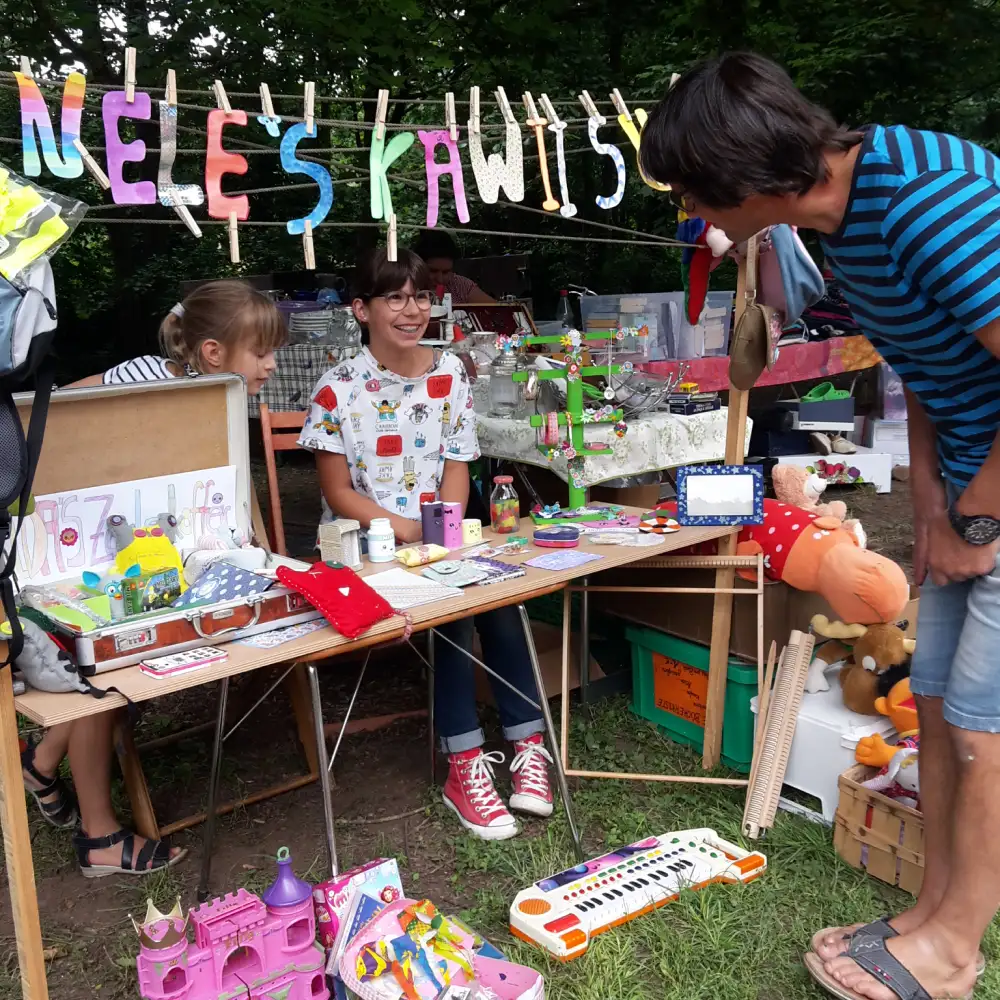 Kind sitzt an einem Tisch und verkauft Spielzeug während eines Flohmarktes