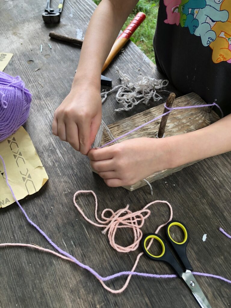Kind bastelt ein Schiff aus Holz und Wolle auf einem Tisch.
